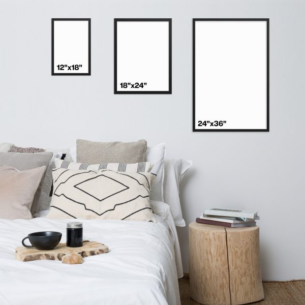 Three framed blank canvases of different portrait sizes above a neatly made bed with a round wooden side table.