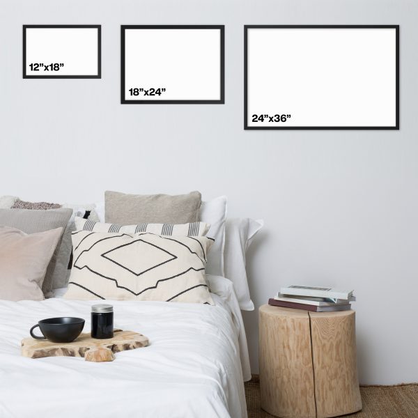 Three framed blank canvases of different landscape sizes above a neatly made bed with a round wooden side table.